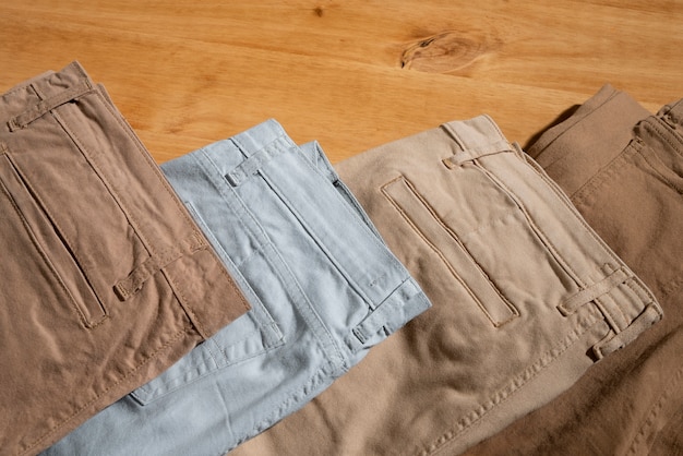 Three pairs of cargo-style pants in beige, light blue, and tan colors folded neatly on a wooden surface.