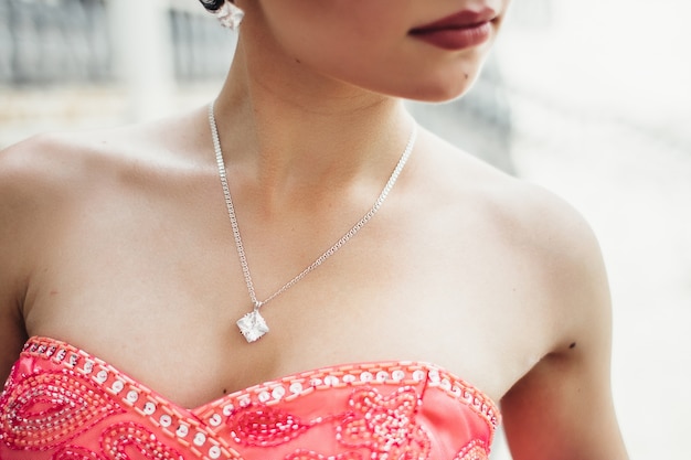 A woman wearing a vibrant red beaded dress and a delicate necklace with a square gemstone pendant.