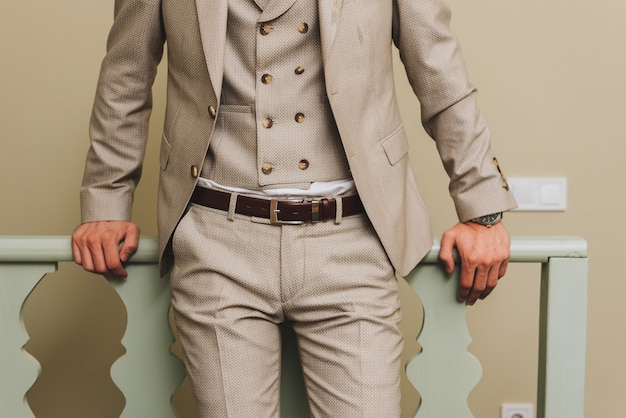 Man in a beige three-piece suit with double-breasted vest, standing by a railing.
