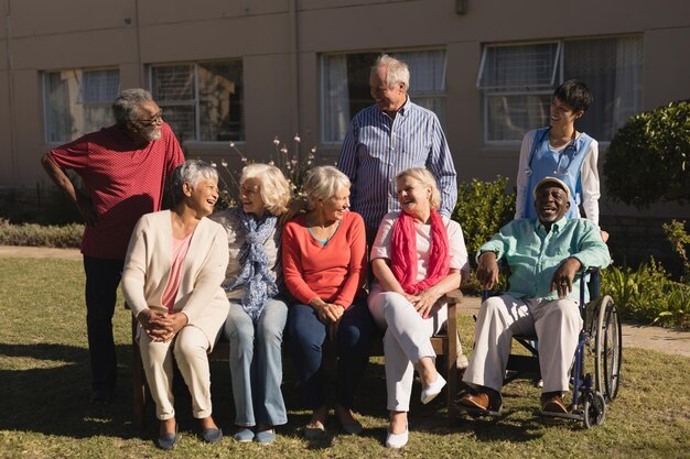 Seniors enjoy time outdoors, sitting on benches and in wheelchairs, laughing and socializing together in a community setting.