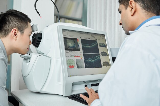 An eye specialist is reviewing retinal scan results on a diagnostic machine while a patient undergoes an advanced eye examination.