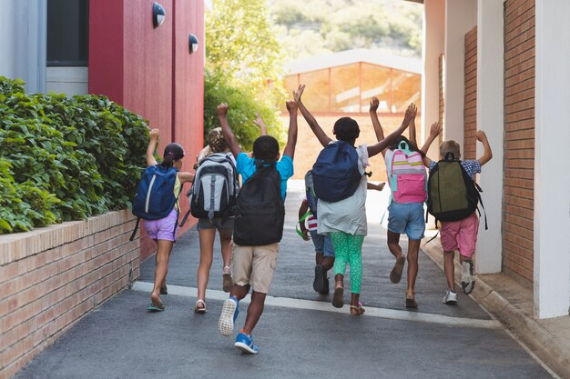 A group of children with backpacks run down a school walkway with their hands raised, celebrating the end of the school day.
