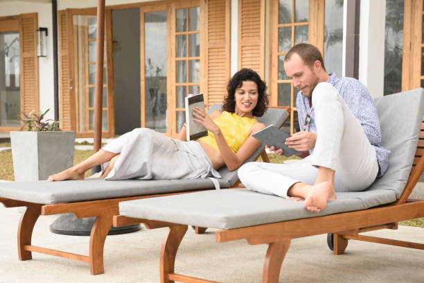 Couple relaxing on outdoor lounge chairs at a resort patio while reading books and enjoying a peaceful vacation moment.