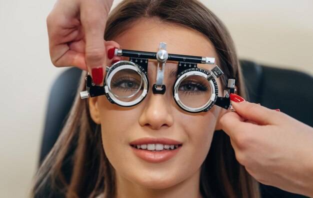 Woman undergoing an eye vision test wearing a trial frame while an optometrist adjusts lenses to measure eyesight accuracy.